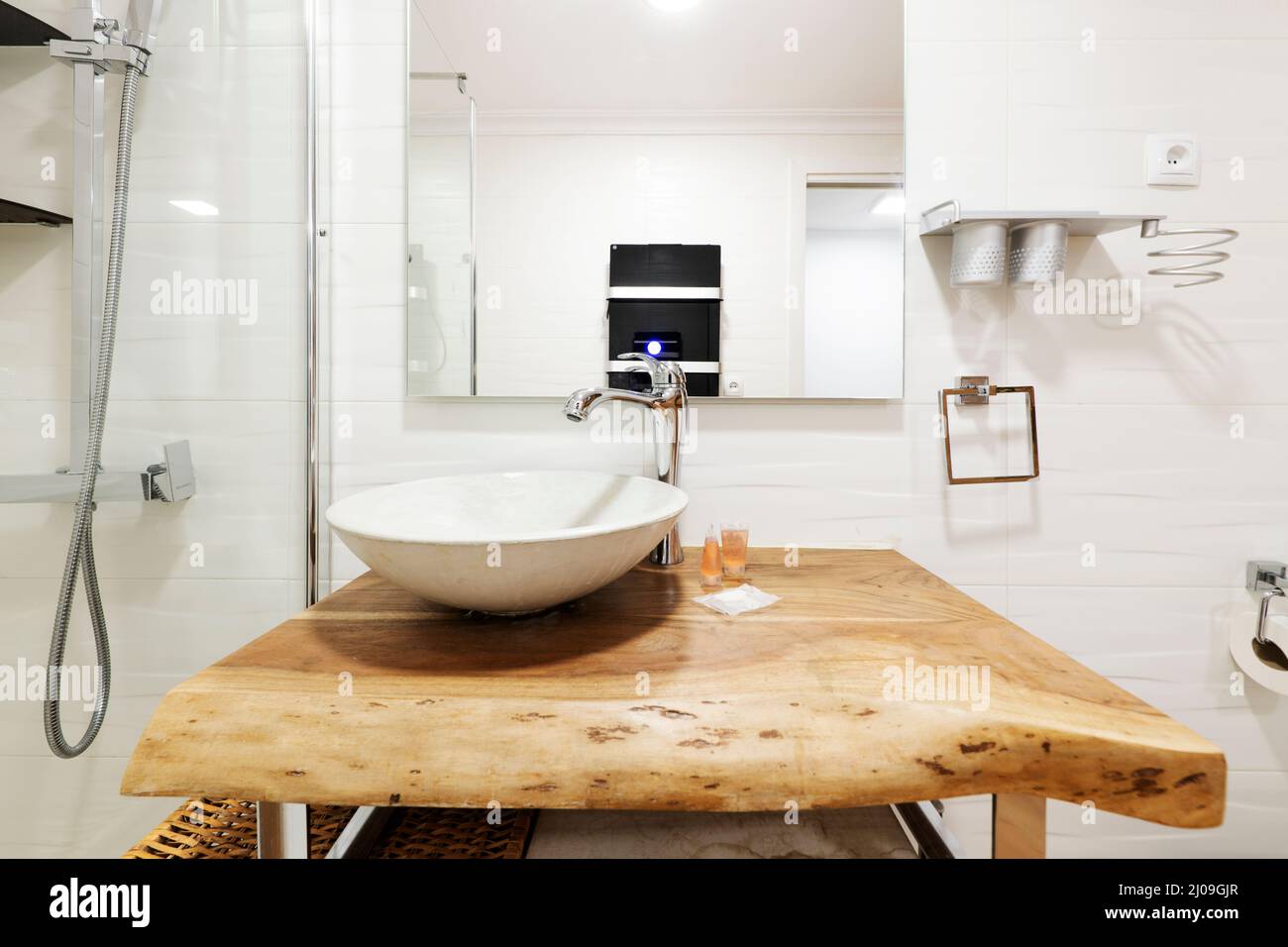 Front image with a white shell sink on a wooden log countertop and a glazed  shower stall, a white anti-fog square mirror Stock Photo - Alamy