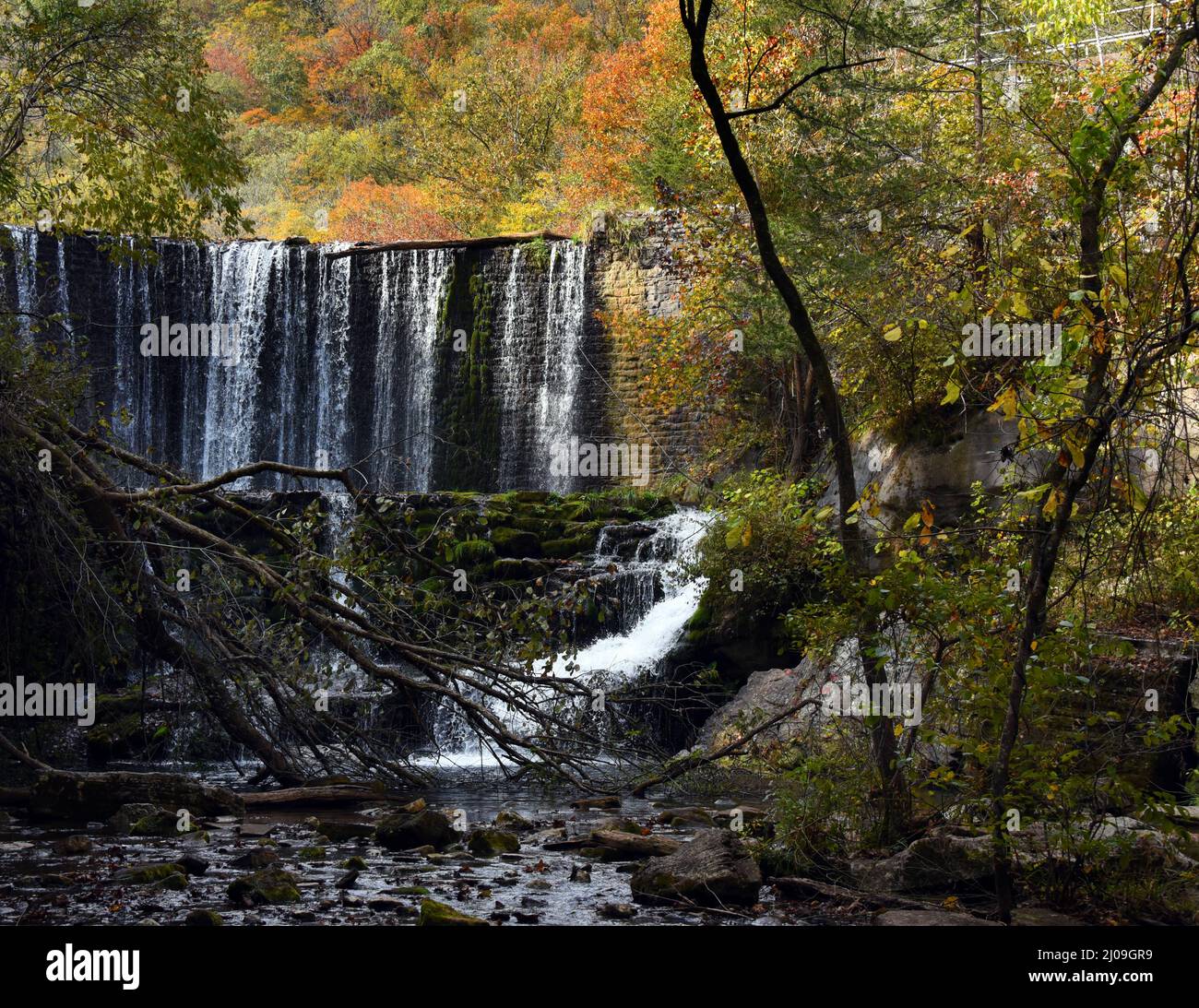 View of the base of Mirror Lake Waterfall.  Stone spillway dams lake but allows water to spill over dam.  Autumn leaves fill the sky at the Blanchard Stock Photo