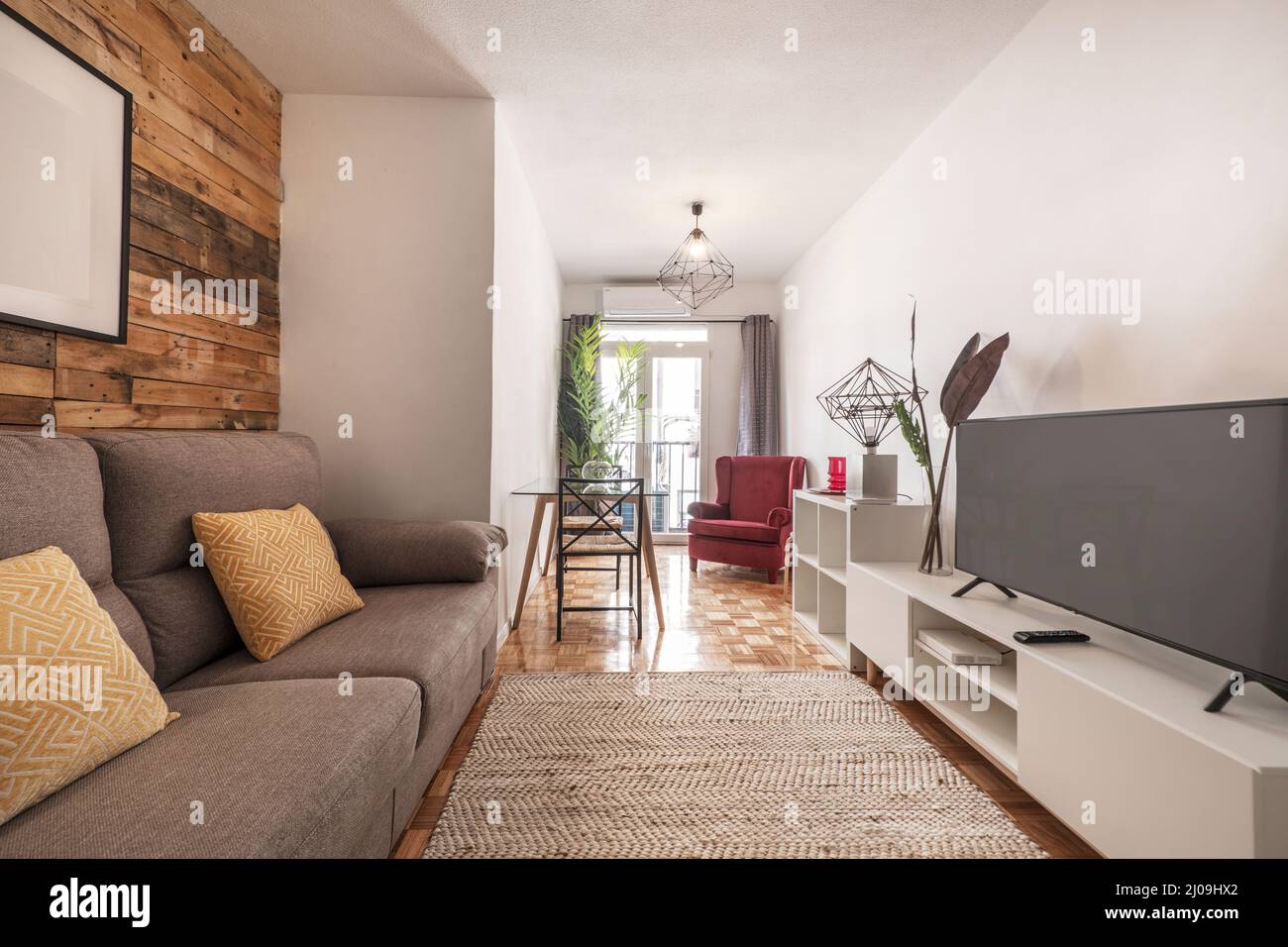 Salón decorado con paredes de madera sin barnizar en apartamento de alquiler a corto plazo con aparador blanco con tv y suelo de parquet de roble, alf Stock Photo