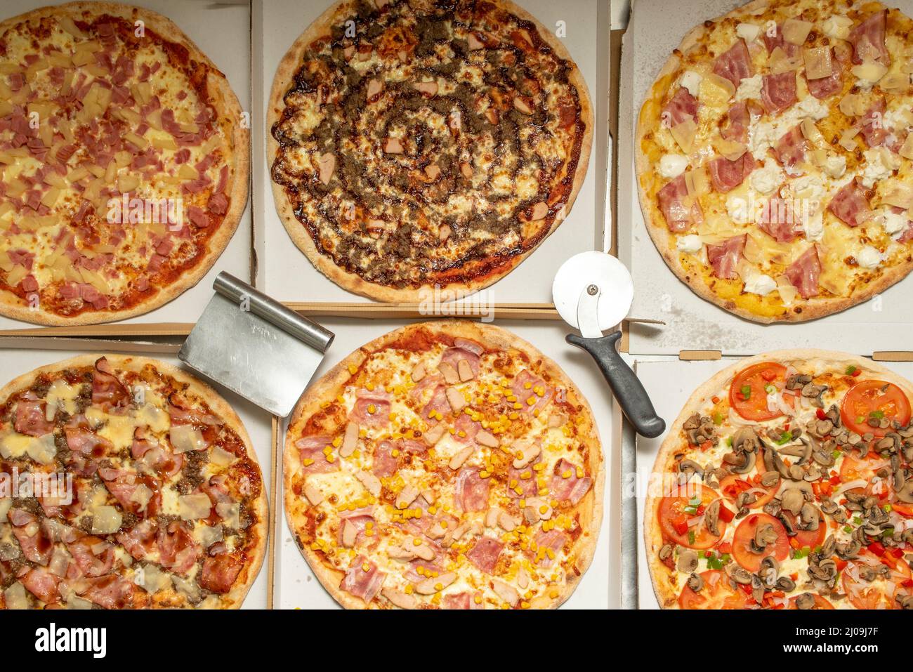 Delicious assorted freshly baked pizzas along with pizza cutters in delivery boxes, Hawaiian, BBQ, Margarita, Bacon and Cheese, Carbonara with guancia Stock Photo
