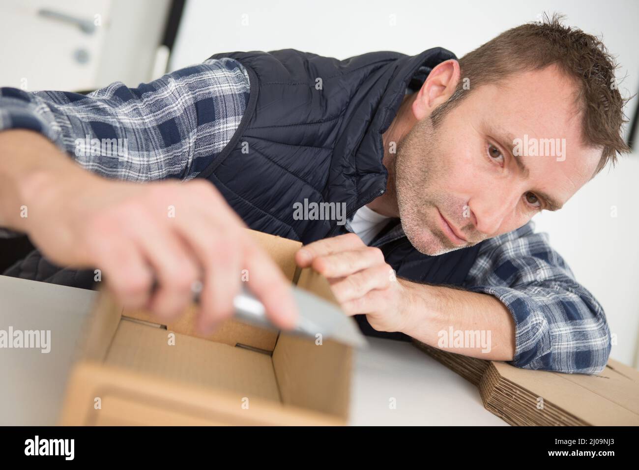 man trimming edge of cardboard container with sharp knife Stock Photo