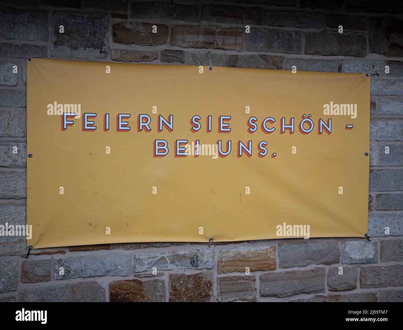 Yellow banner with 'feiern sie schon bei uns' (have fun with us) text on a brick wall Stock Photo