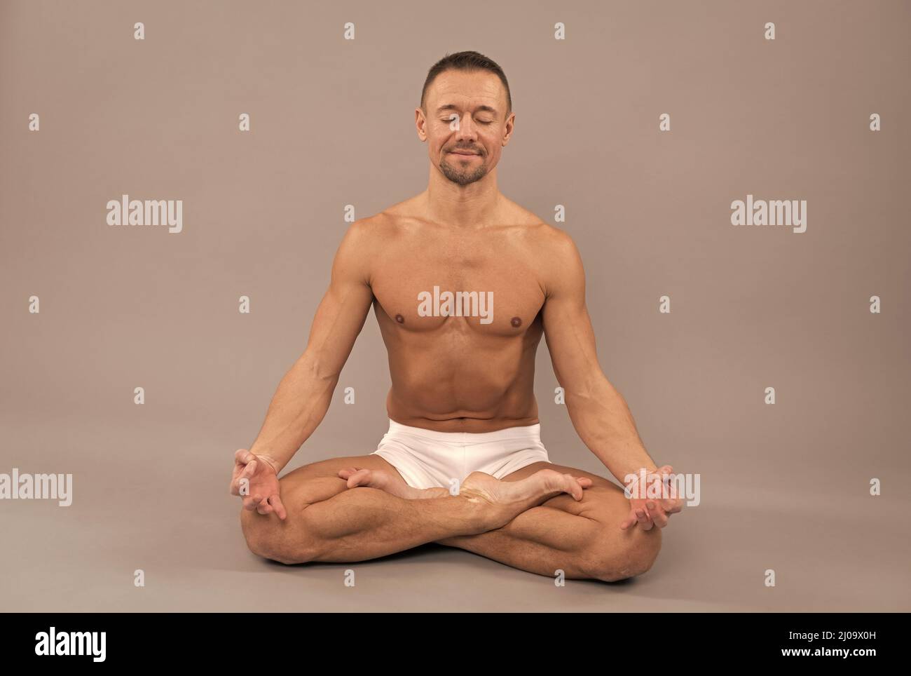 Yogi man meditate sitting in lotus yoga position grey background, meditation Stock Photo