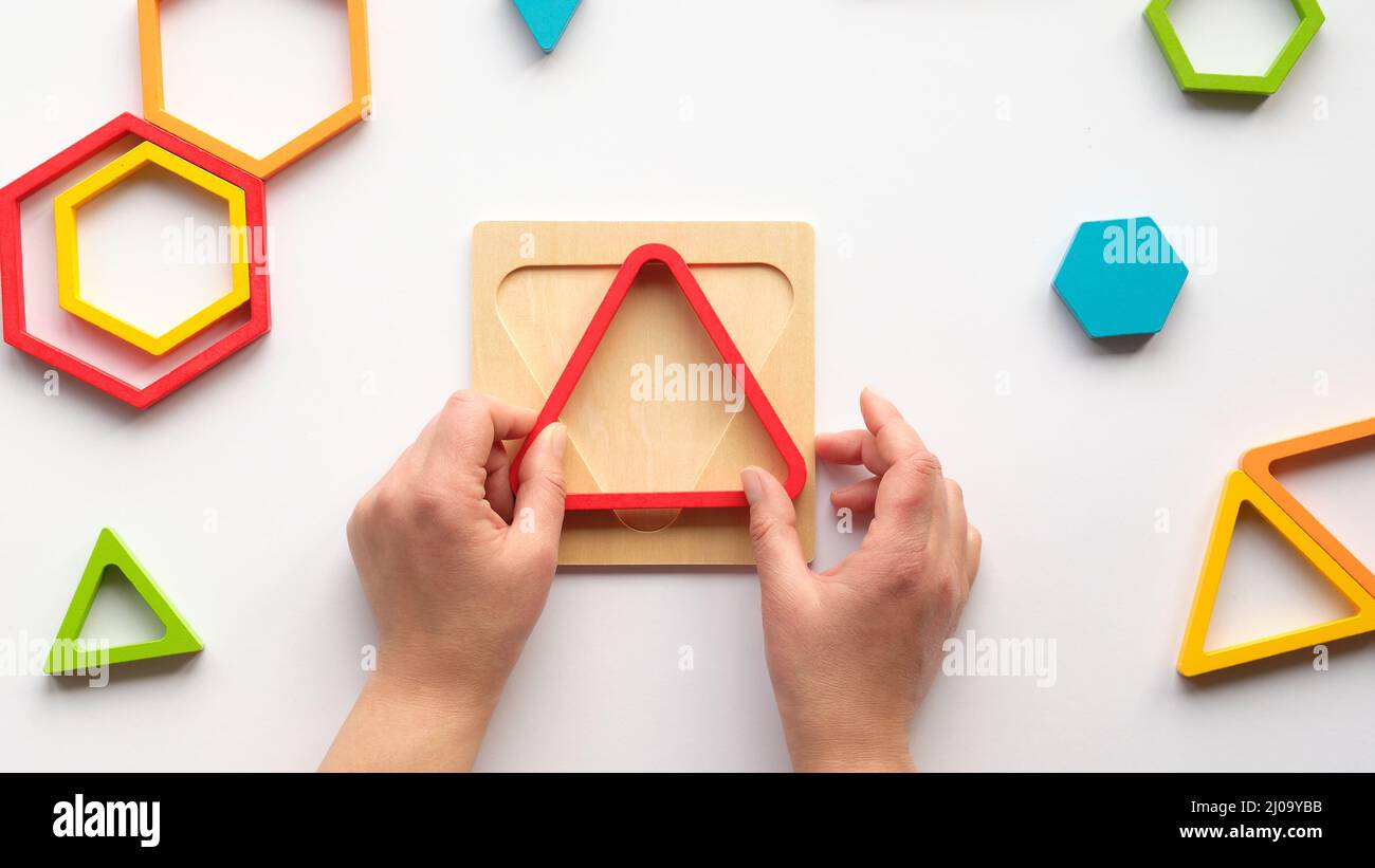 Hands with triangle. Nested wood triangles and hexagons, concentric figures. Stacking puzzle. Stock Photo