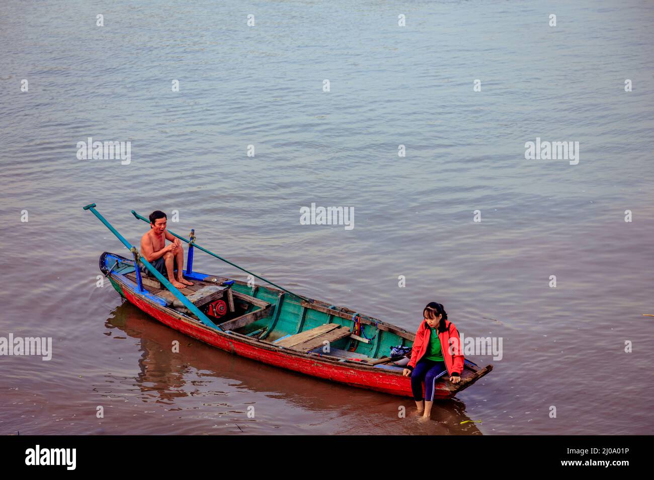 Just off the banks of the Mekong River two people sit in their wood row boat by Chau Doc. Stock Photo