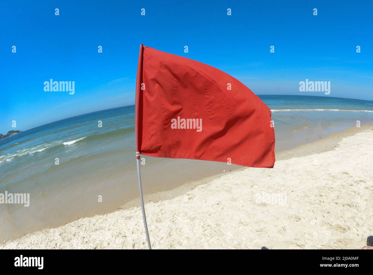 red flag on the beach indicating danger zone for swimming, in a blue