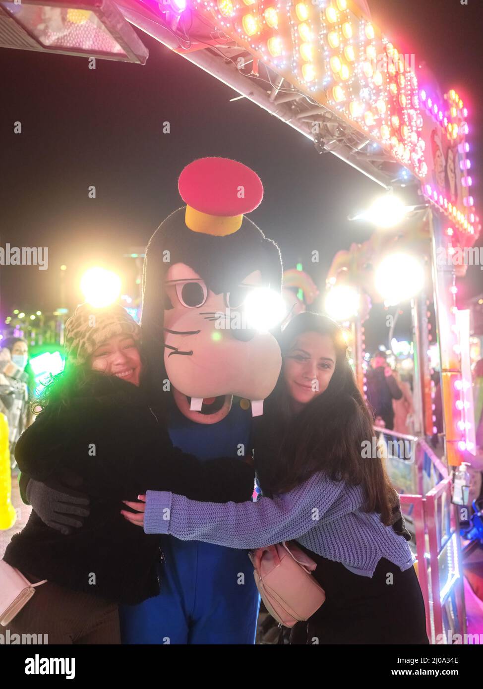 Girls embracing an actor dressed like Goofy dog in a theme park at night Stock Photo