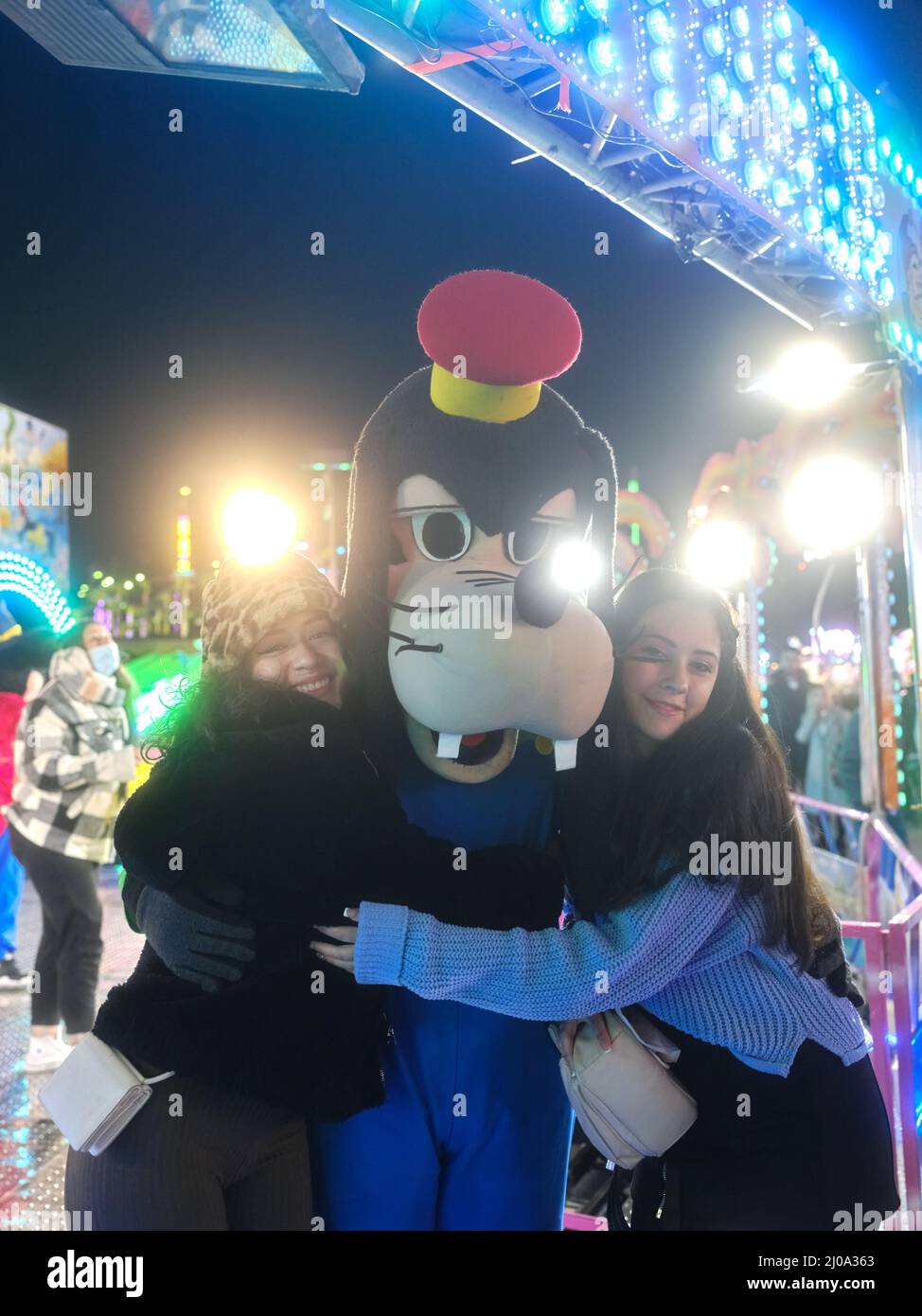 Two women embracing an actor dressed like a character of a dog in a theme park Stock Photo