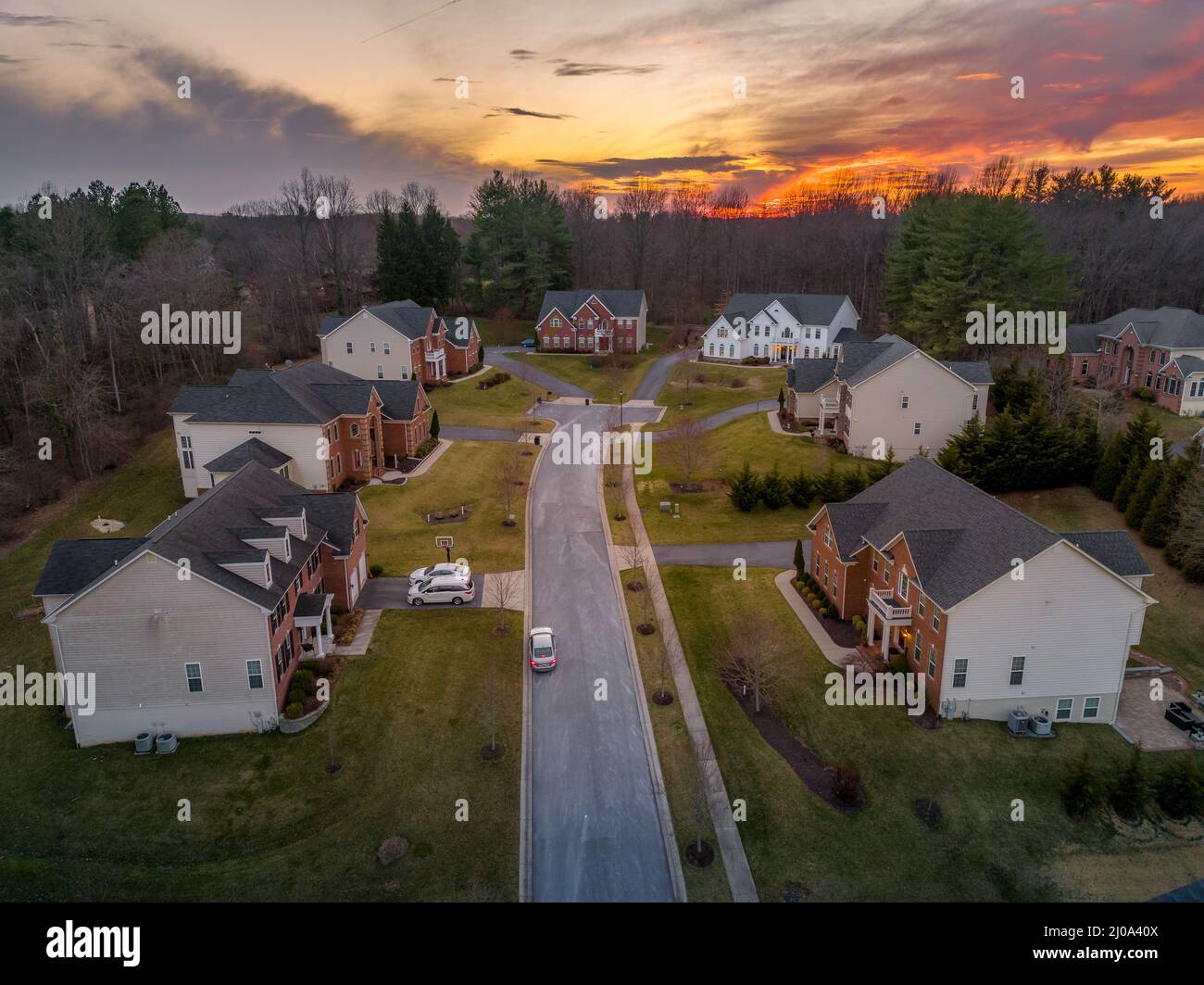 Curving road leading to a dead end neighborhood with colorful orange evening sun is setting over upper class East Coast American neighborhood cul-de-s Stock Photo