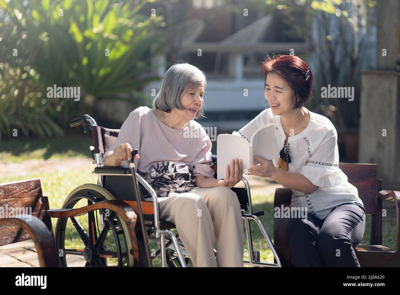 Elderly woman and daughter reading a book together in backyard. Stock Photo