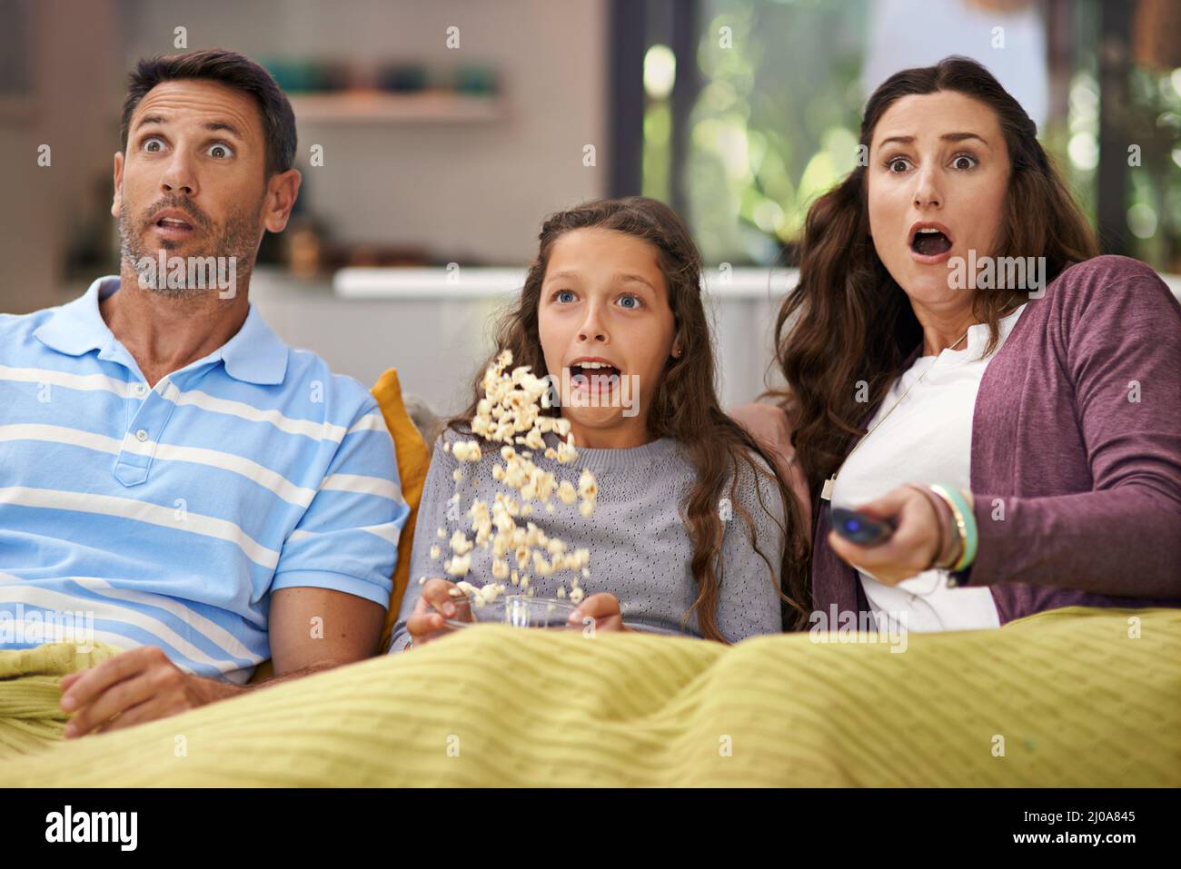 They love scary movies. Shot of a family sitting on their living room sofa watching a movie and eating popcorn. Stock Photo