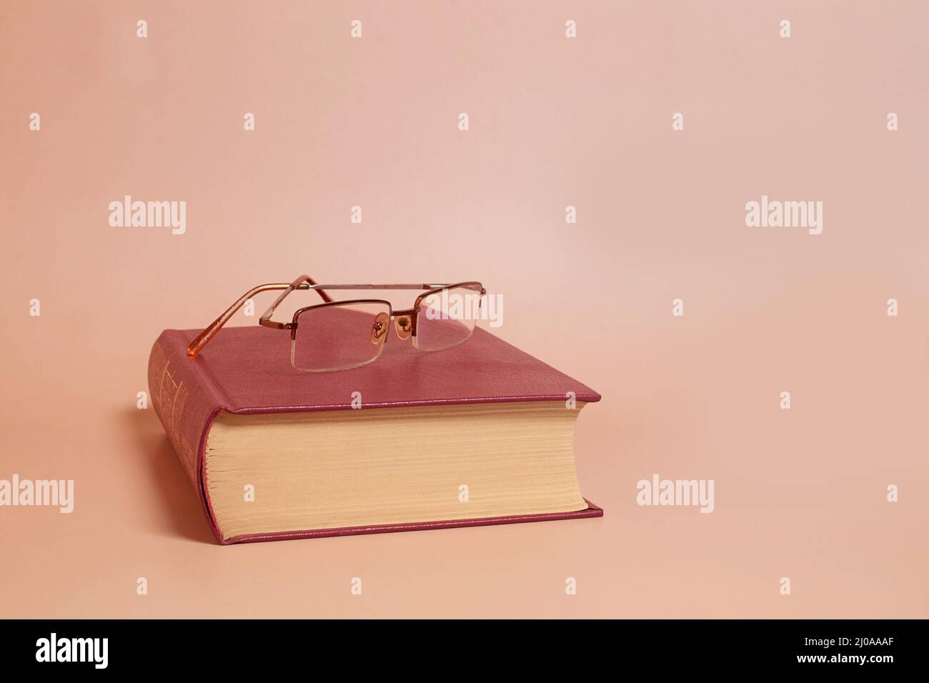 Reading glasses lie on a thick book, colored background. Side view Stock Photo