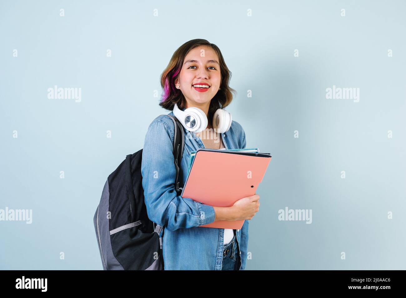 Young Hispanic student woman wearing backpack and holding books over isolated blue background Stock Photo