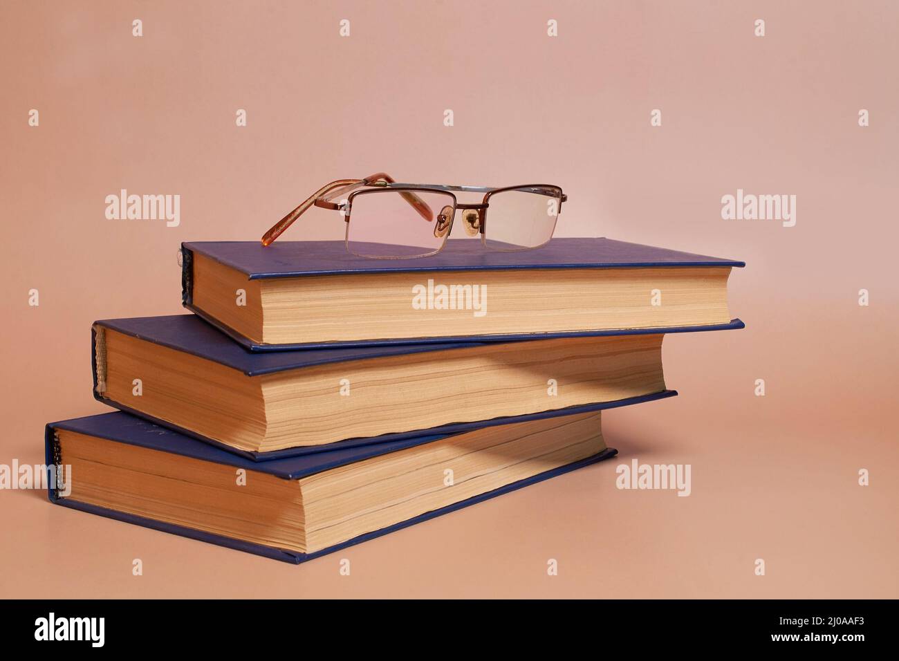 Reading glasses are on a stack of books on a colored background. Side view Stock Photo