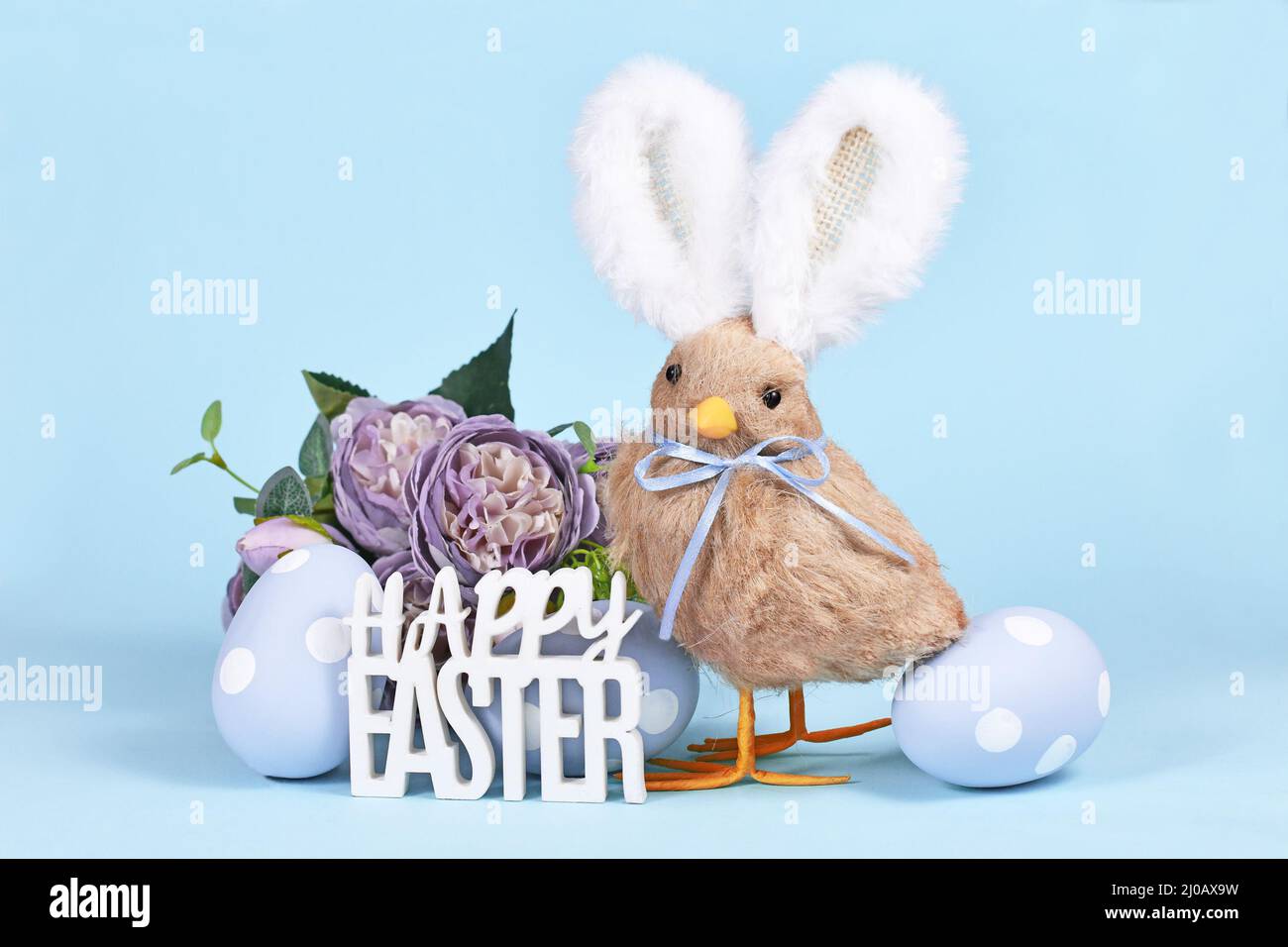 Easter chick with bunny ears, painted eggs and text 'Happy Easter' on blue background Stock Photo