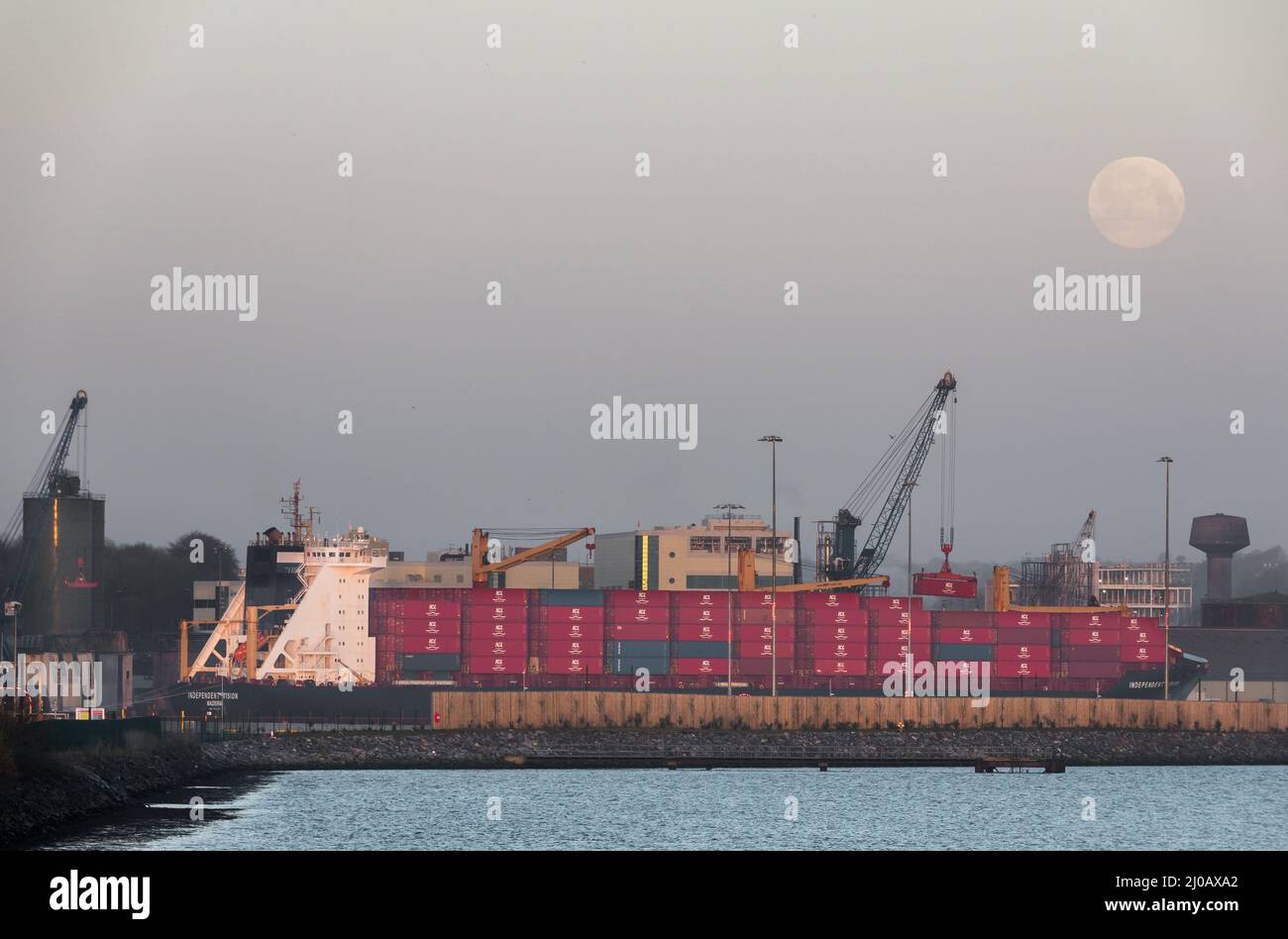 Ringaskiddy, Cork, Ireland. 18th March, 2022. A worm Moon desends as container vessel Independent vision loads with a cargo bound for Chester, USA at Ringaskiddy docks, Co. Cork, Ireland.  - Credit; David Creedon / Alamy Live News Stock Photo