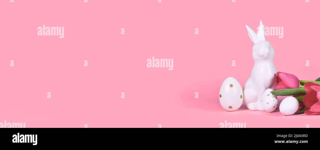 Banner with easter bunny, white eggs with golden dots and tulip spring flowers on pink background with copy space Stock Photo