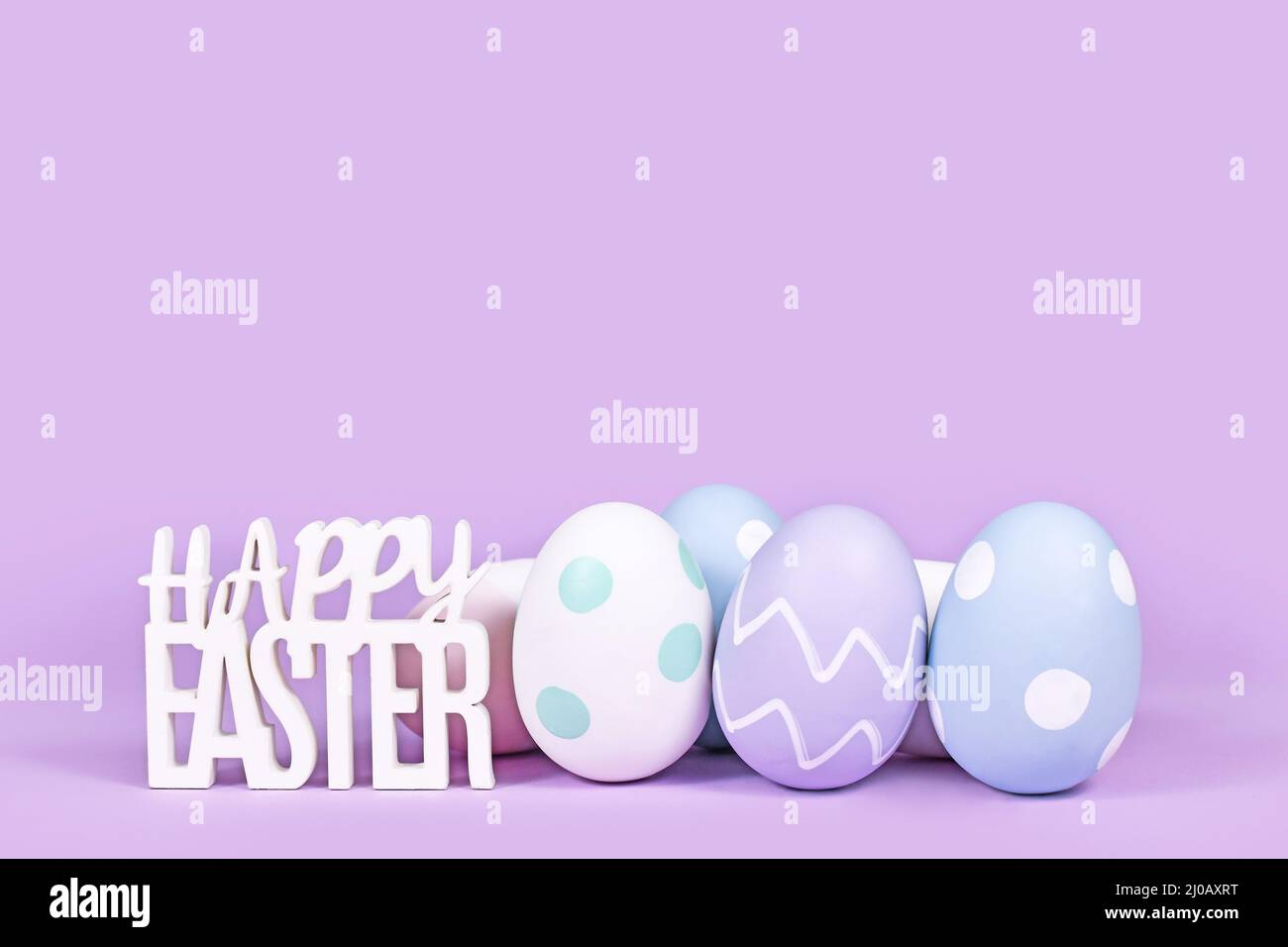Pastel colored easter eggs and text 'Happy Easter' on violet background with copy space Stock Photo