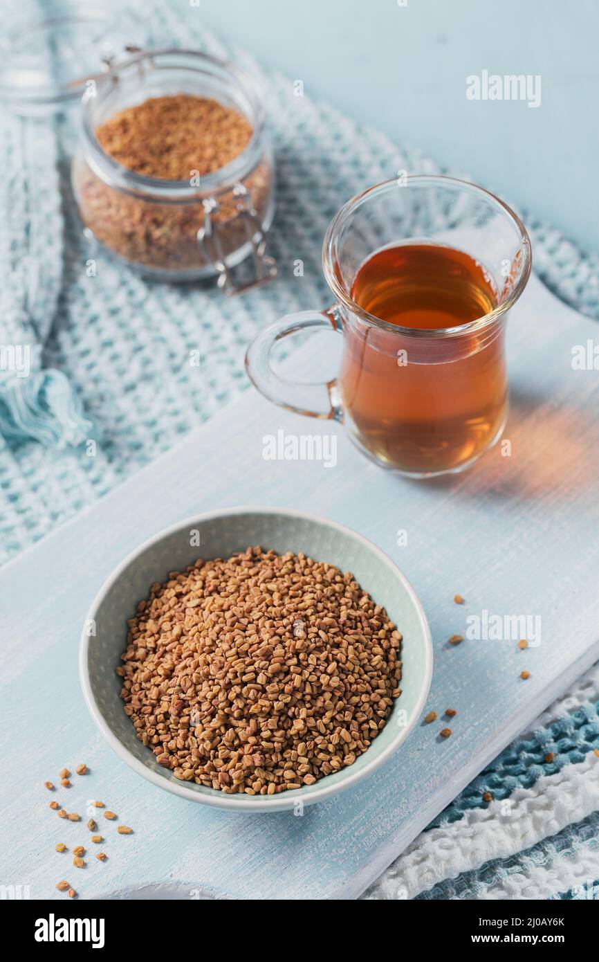 Glass of Egyptian fenugreek yellow tea, Helba or Methi Dana drink and fenugreek seeds on light blue background Stock Photo