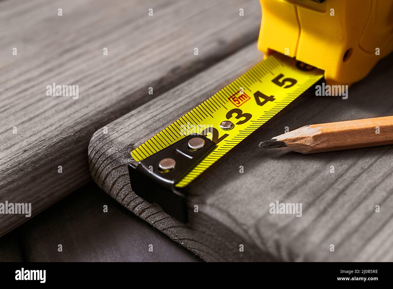 Hands in gloves of joiner in carpentry. Carpenter is measuring length of wood planks or timbers