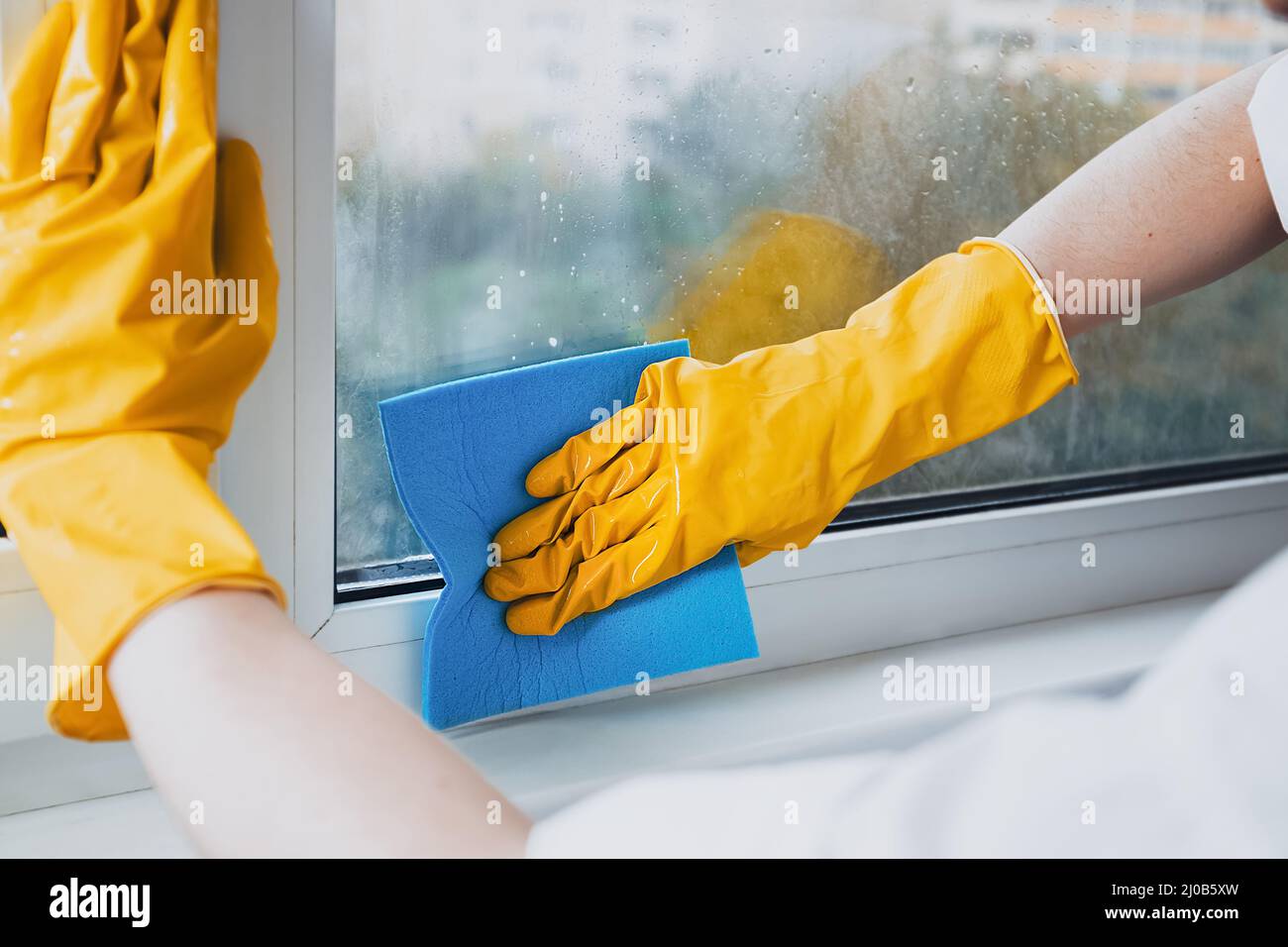 Man in yellow rubber gloves cleaning window glasse with cleaner spray
