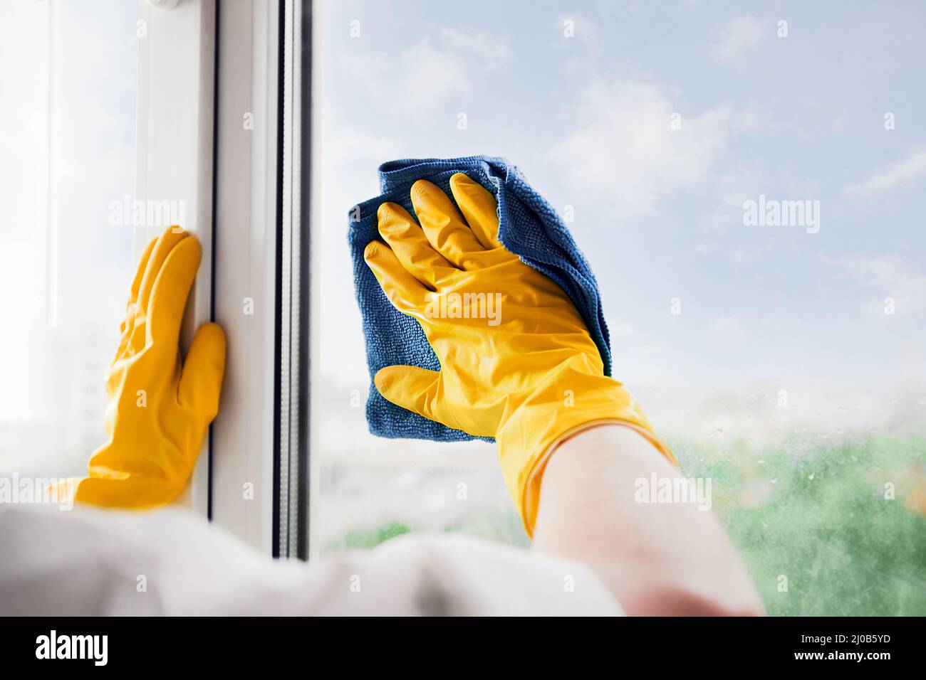 Man in yellow rubber gloves cleaning window glasse with cleaner spray