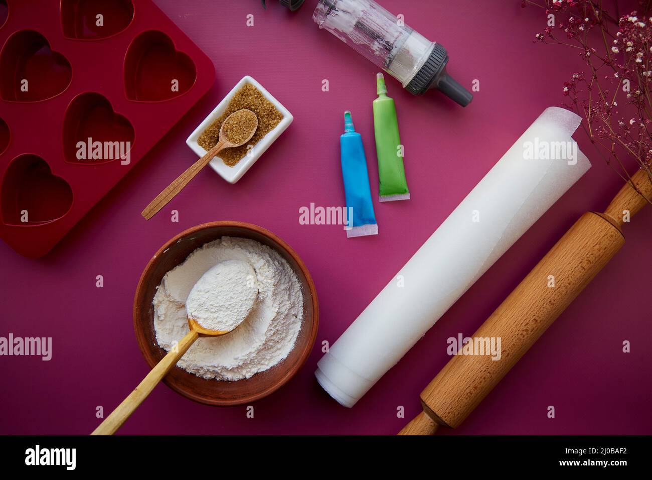Baking tools complete with heart-shaped silicone mold, rolling pin, confectionery syringe, glaze, flour, sugar. View from above. Stock Photo