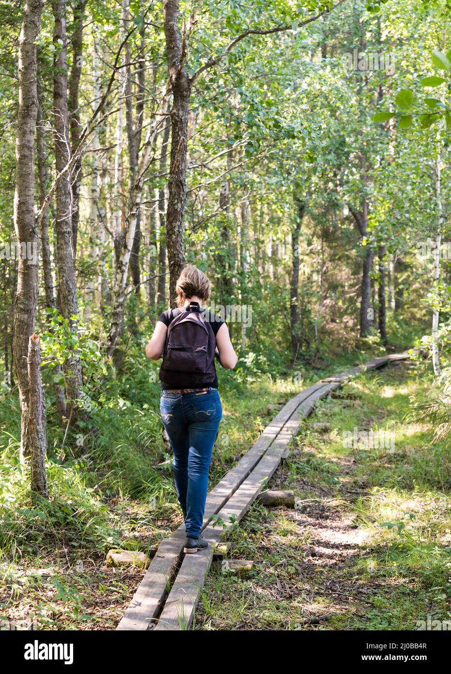 Young healthy woman with backpack walking over a wooden path in the Florarna Naturreservat , a Swedish Nature Reserve Park Stock Photo