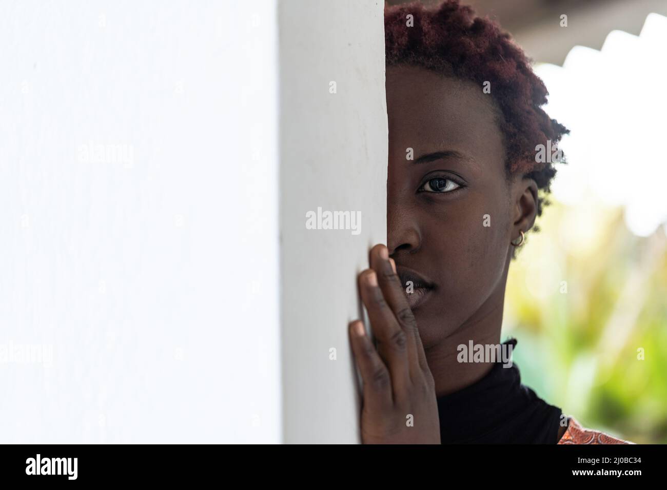 Half face portrait of a beautiful young African girl with short curly hair and a pensive expression on her face leaning against a wall Stock Photo