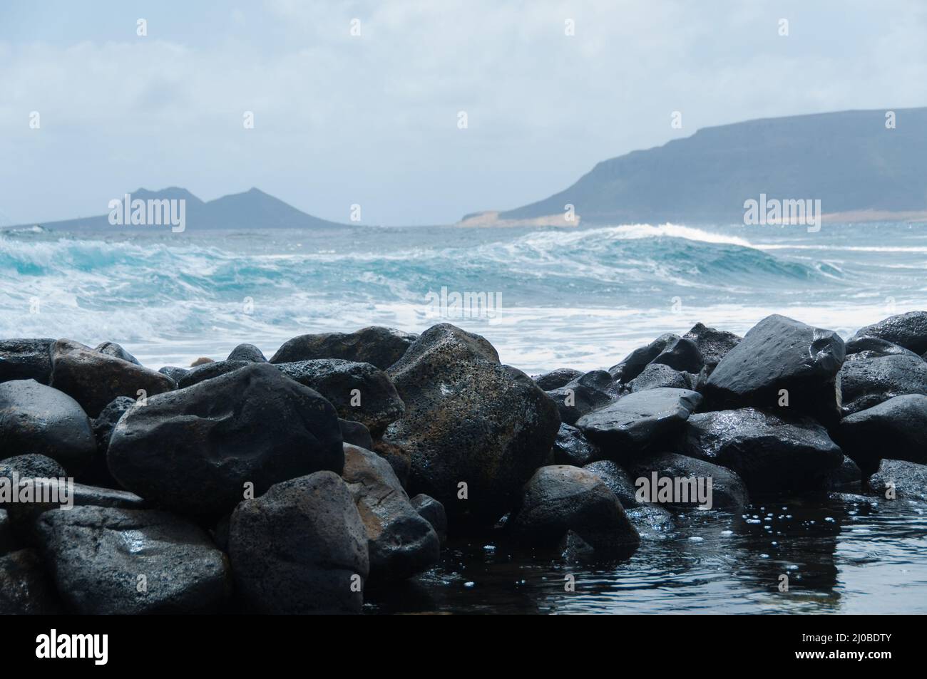 Black rock stone coast in front of rough windy sea with waves Stock Photo