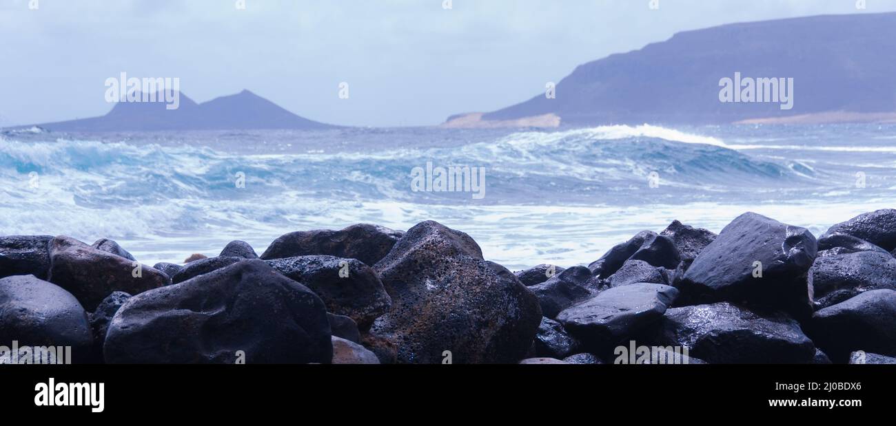 Black rock stone coast in front of rough windy sea with waves Stock Photo