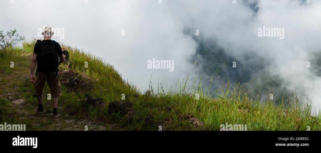 White man with black shirt and hat walking along a cliff above the clouds on mountain in cape verde Stock Photo