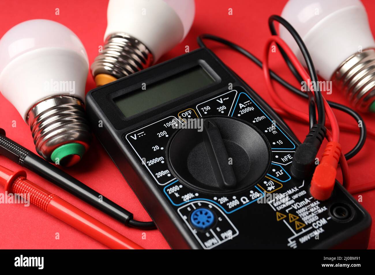 Multimeter and energy saving bulbs on red background Stock Photo