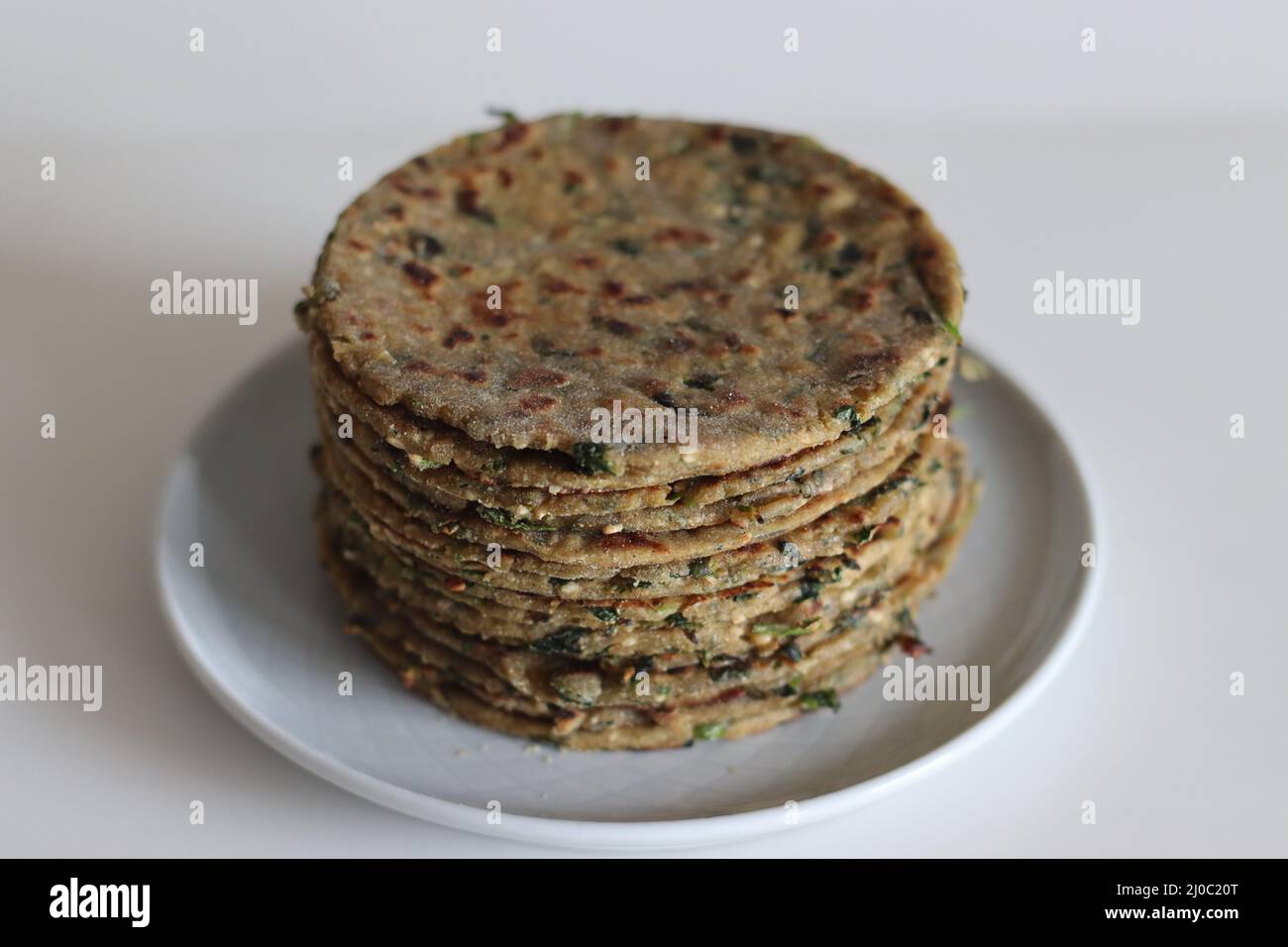 Bajra methi thepla. Indian flat bread made of pearl millet flour, fenugreek leaves, sesame seeds, yogurt and spices. Shot on white background. Stock Photo