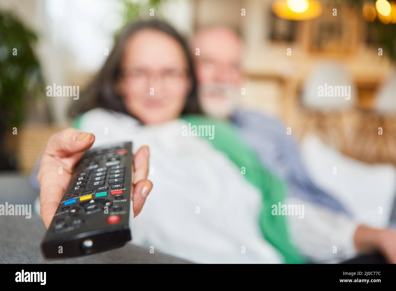 Elderly woman holds the TV remote control in her hand as a symbol for