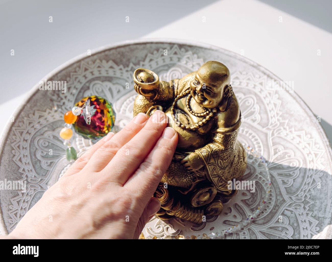 Person hand rubbing small golden laughing Buddha figurine tummy. It believed to bring happiness, good fortune and wealth. Buddai monk. Stock Photo