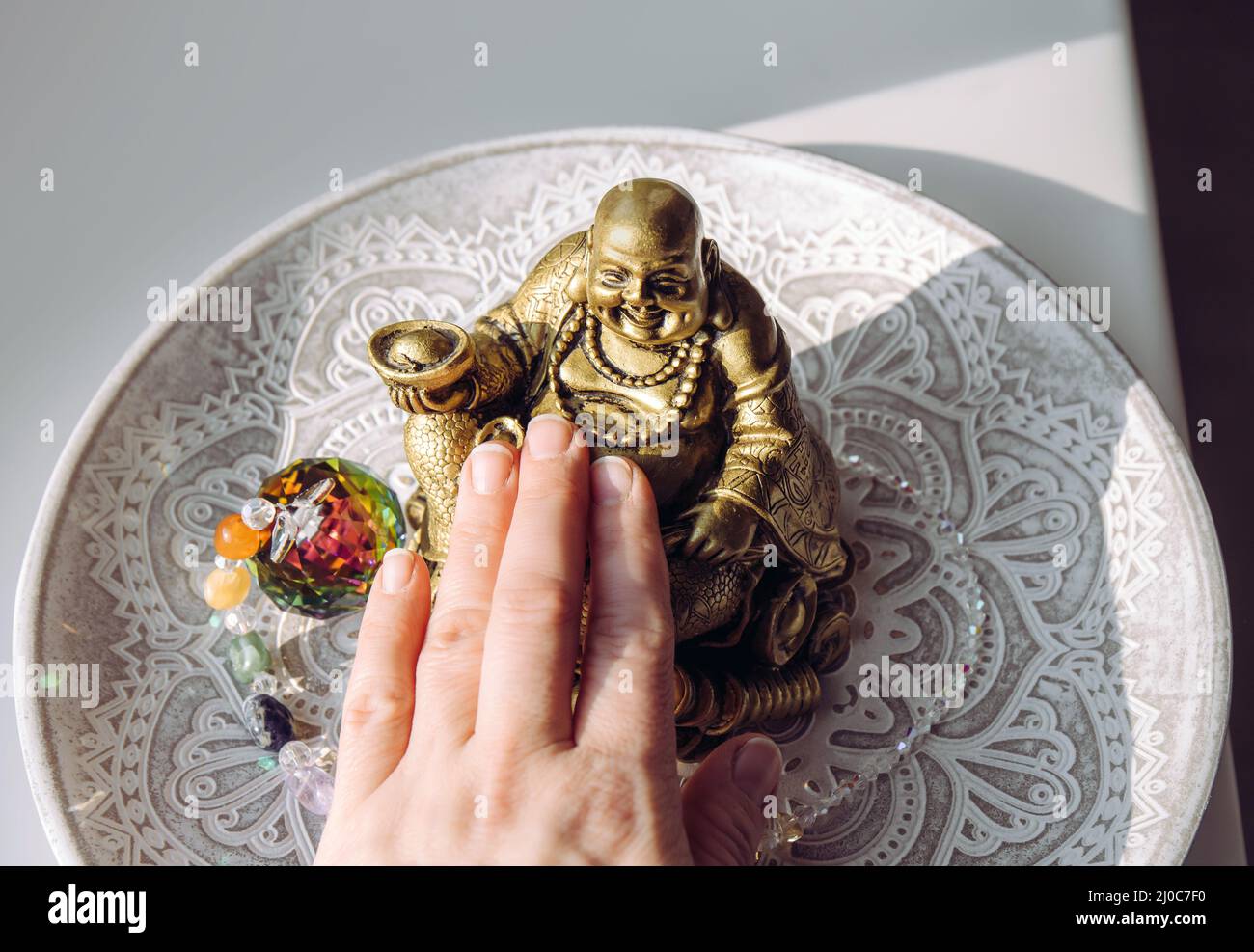 Person hand rubbing small golden laughing Buddha figurine tummy. It