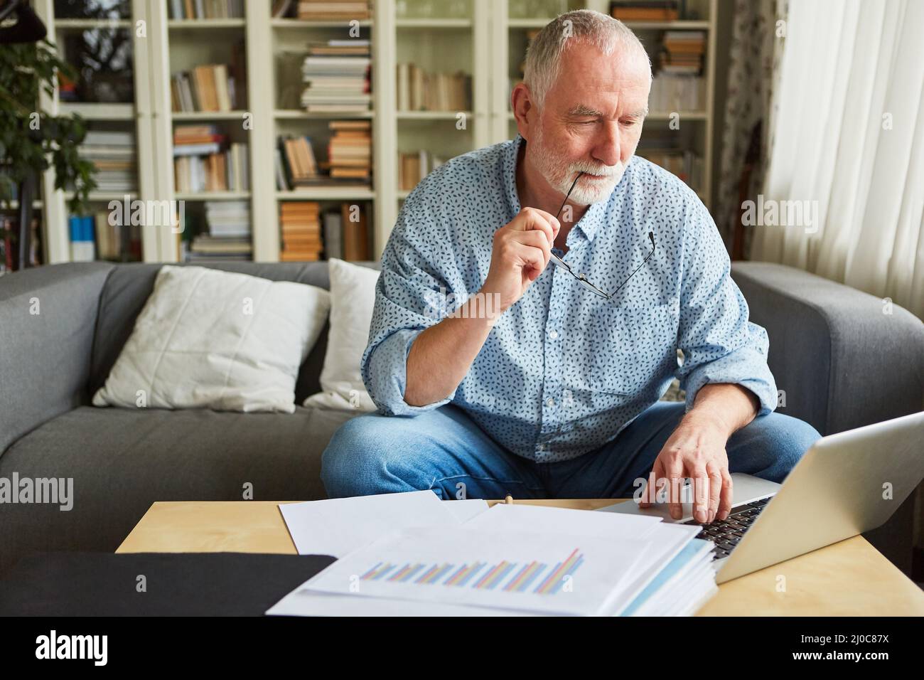 Pensive senior man doing accounting or working on tax return on laptop computer Stock Photo