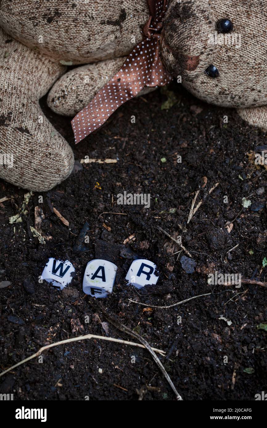 rustic style teddy bear on muddy soil with the word war written in letter dice, illustrating a childhood during a time of war Stock Photo