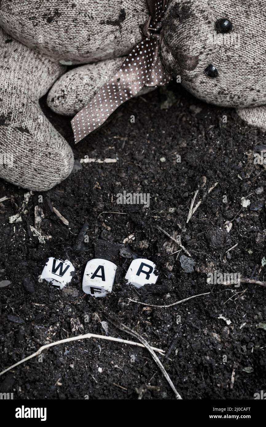 rustic style teddy bear on muddy soil with the word war written in letter dice, illustrating a childhood during a time of war Stock Photo