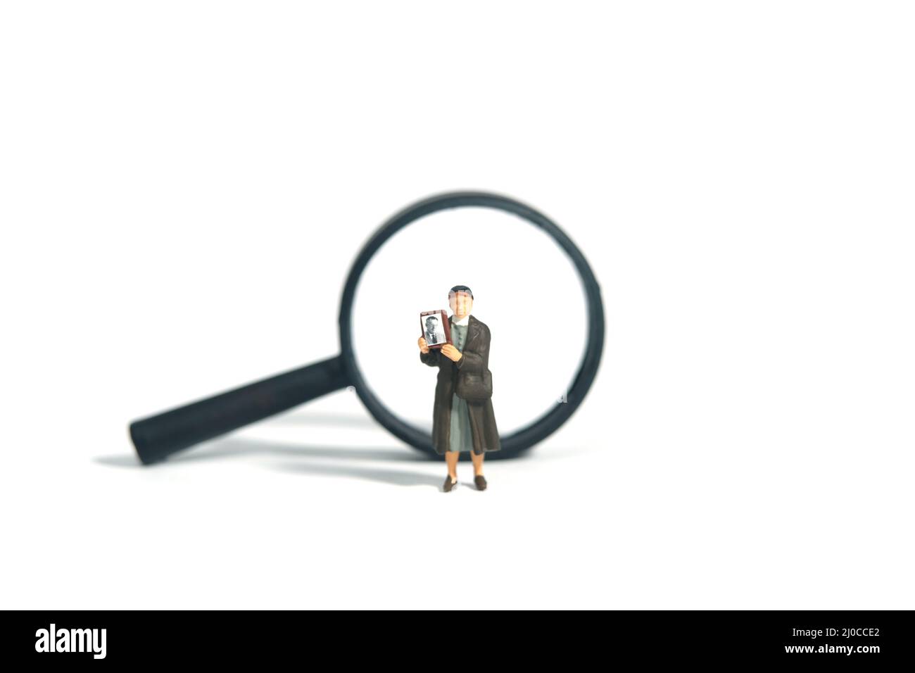 Miniature people toy figure photography. A woman holding photo frame standing above magnifying glass, searching missing person. Isolated white backgro Stock Photo