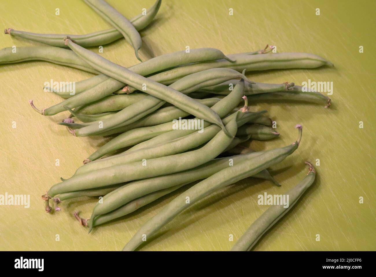 Untrimmed Green bean vegetables on a green chopping board Stock Photo
