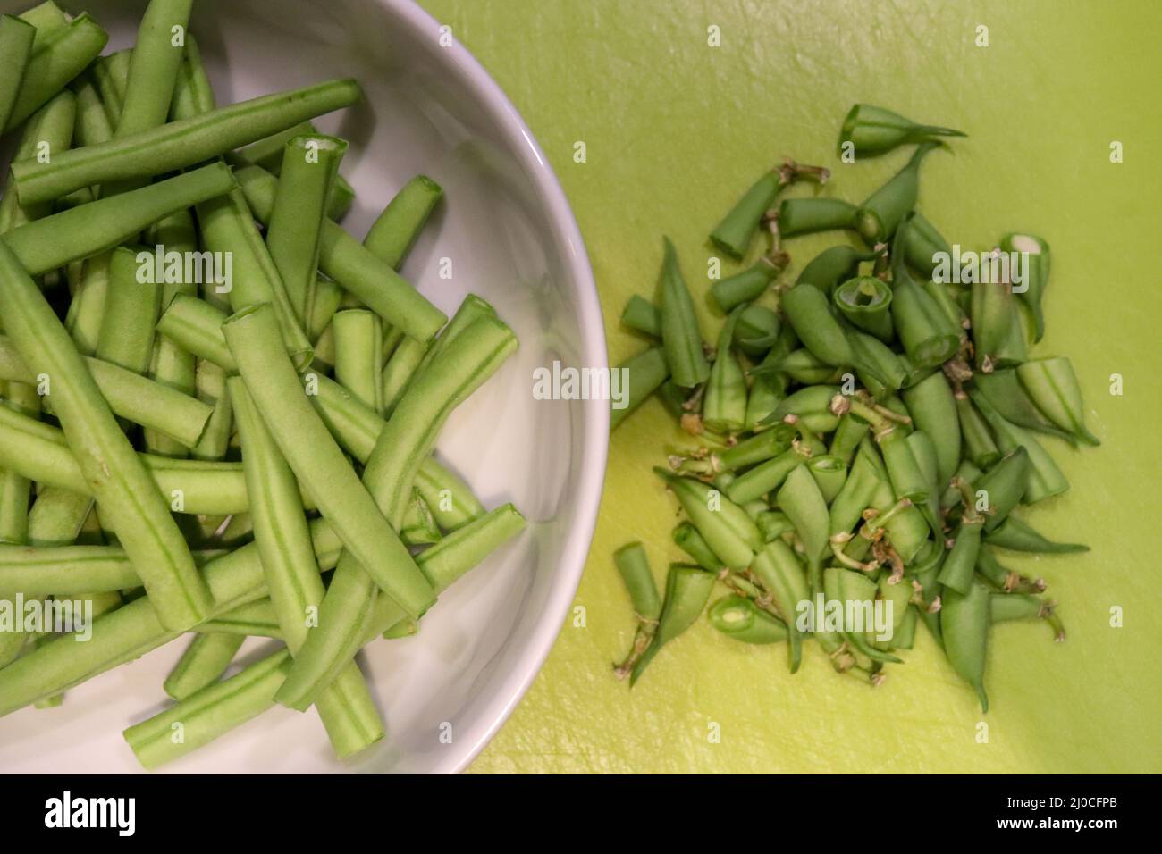 Trimmed bean vegetables in a white bowl and trimmed parts on a chopping board Stock Photo