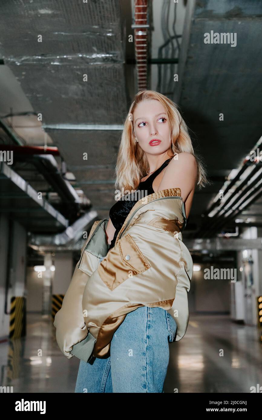 Fashionable blonde female with goldish-colored jacket in a parking garage Stock Photo