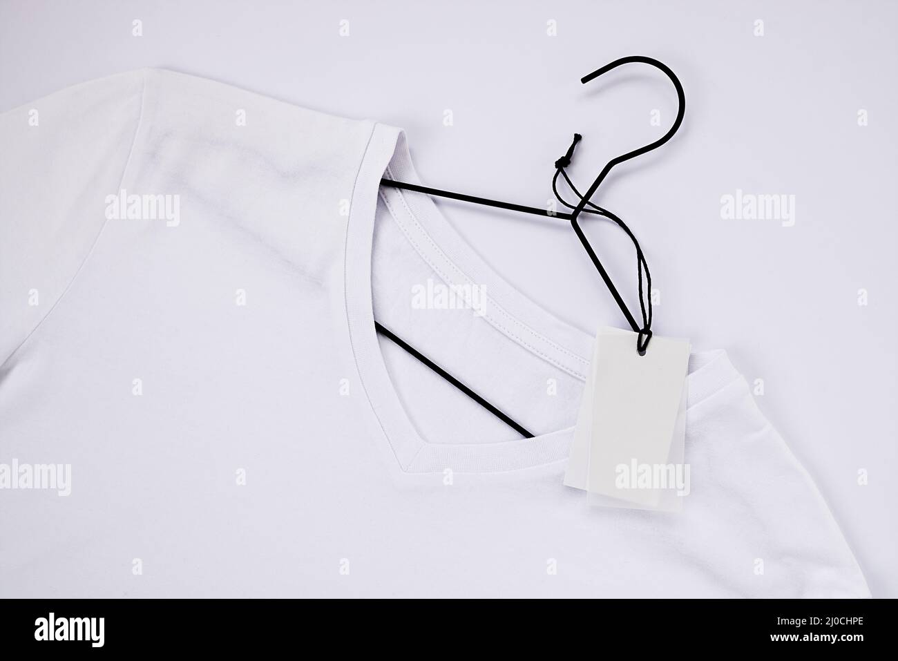 White cotton t-shirt mockup, on a black hanger. Close-up, white tag for logo, label Stock Photo