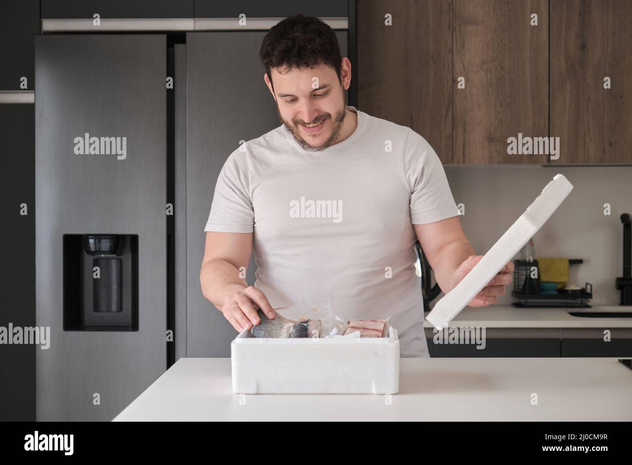 Young latin man opening his weekly delivery of fish in an EPS isothermal box. Stock Photo