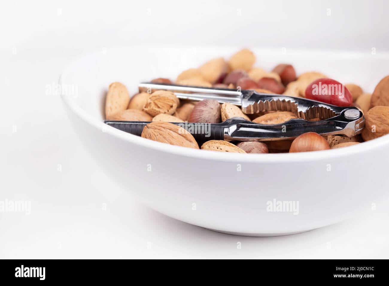 Variety of shelled nuts with nutcracker pliers in a bowl, close up. Pile of unsalted walnuts, pecans, almonds and hazelnuts in shell. Healthy fat conc Stock Photo
