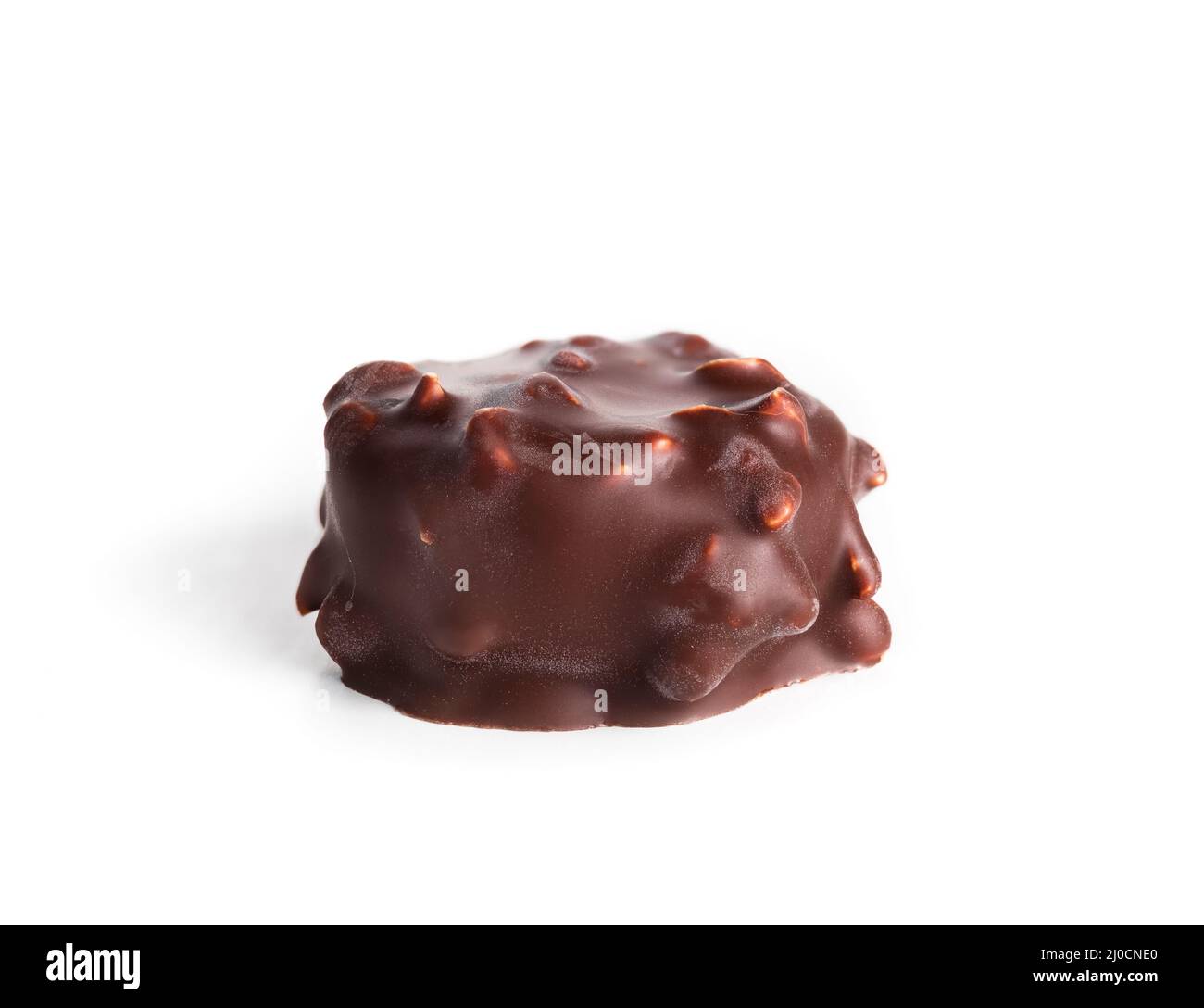 Isolated chocolate praline with hazelnut pieces. Closeup of one small non uniform chocolate truffle piece coated with dark chocolate. Selective focus. Stock Photo