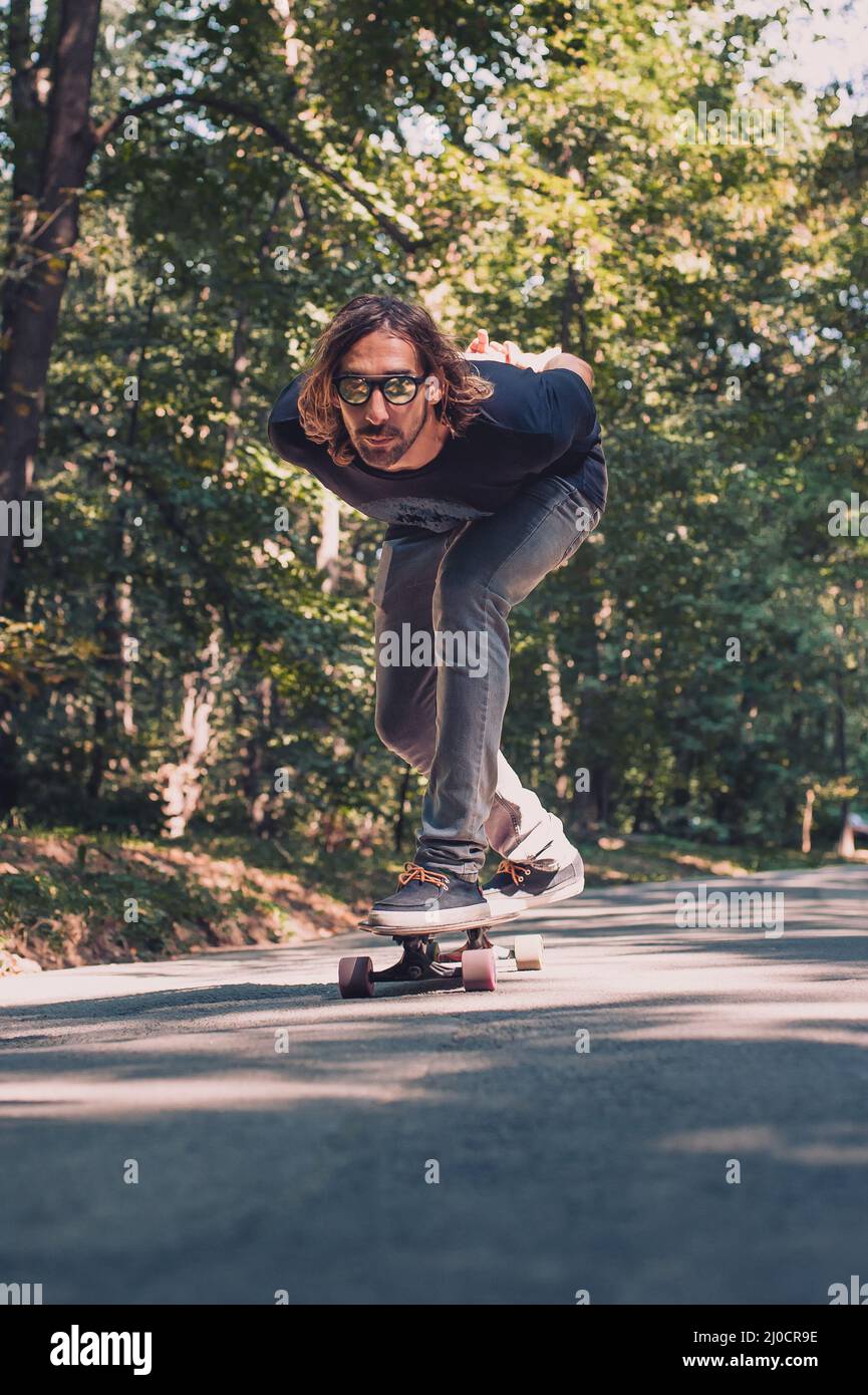Skateboarder ride a longboard skateboard on the road through the forest.  Freeride longboard skating Stock Photo - Alamy