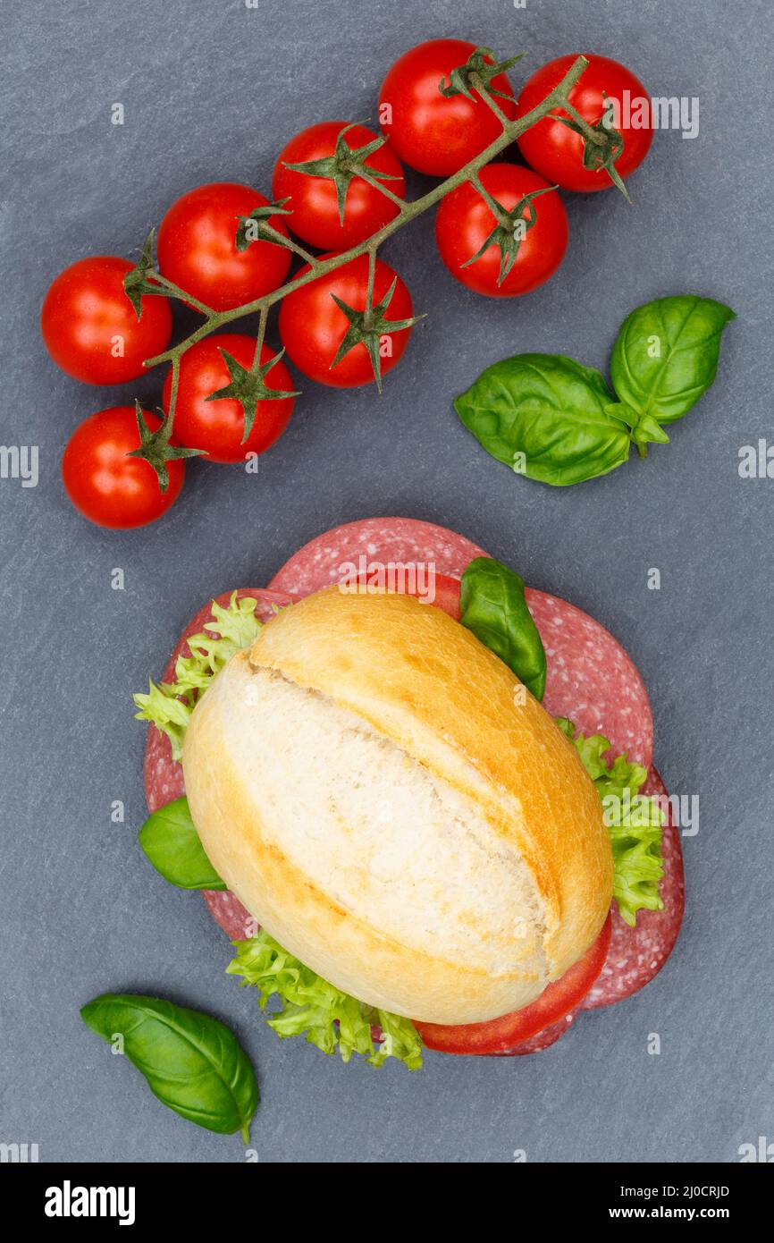 Roll sandwich baguette topped with salami ham portrait from above slate